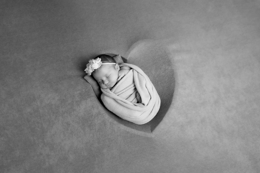 A sleeping figure curled up in a white dress on a gray background, viewed from above in black and white.