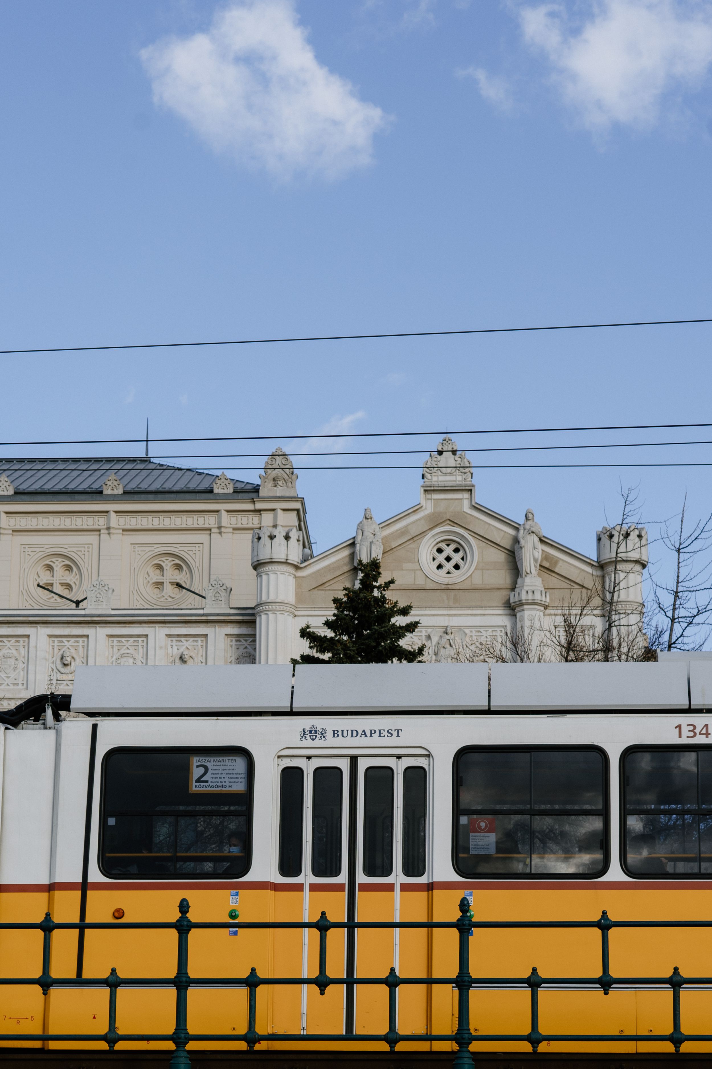 Yellow tram passes in front of an ornate historical building with classical architectural details in Budapest.