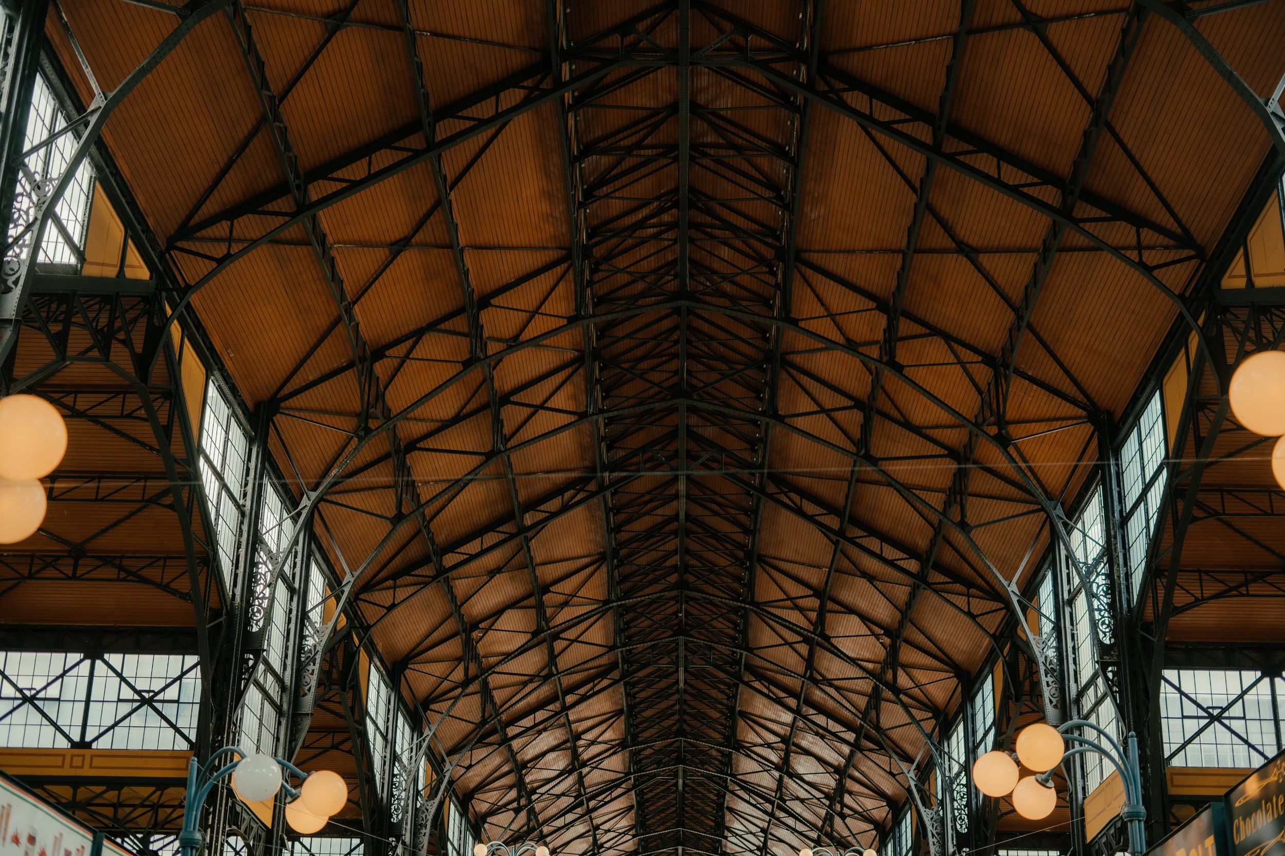 Interior view of historic market hall with ornate iron roof trusses and hanging globe lights creating warm ambiance.
