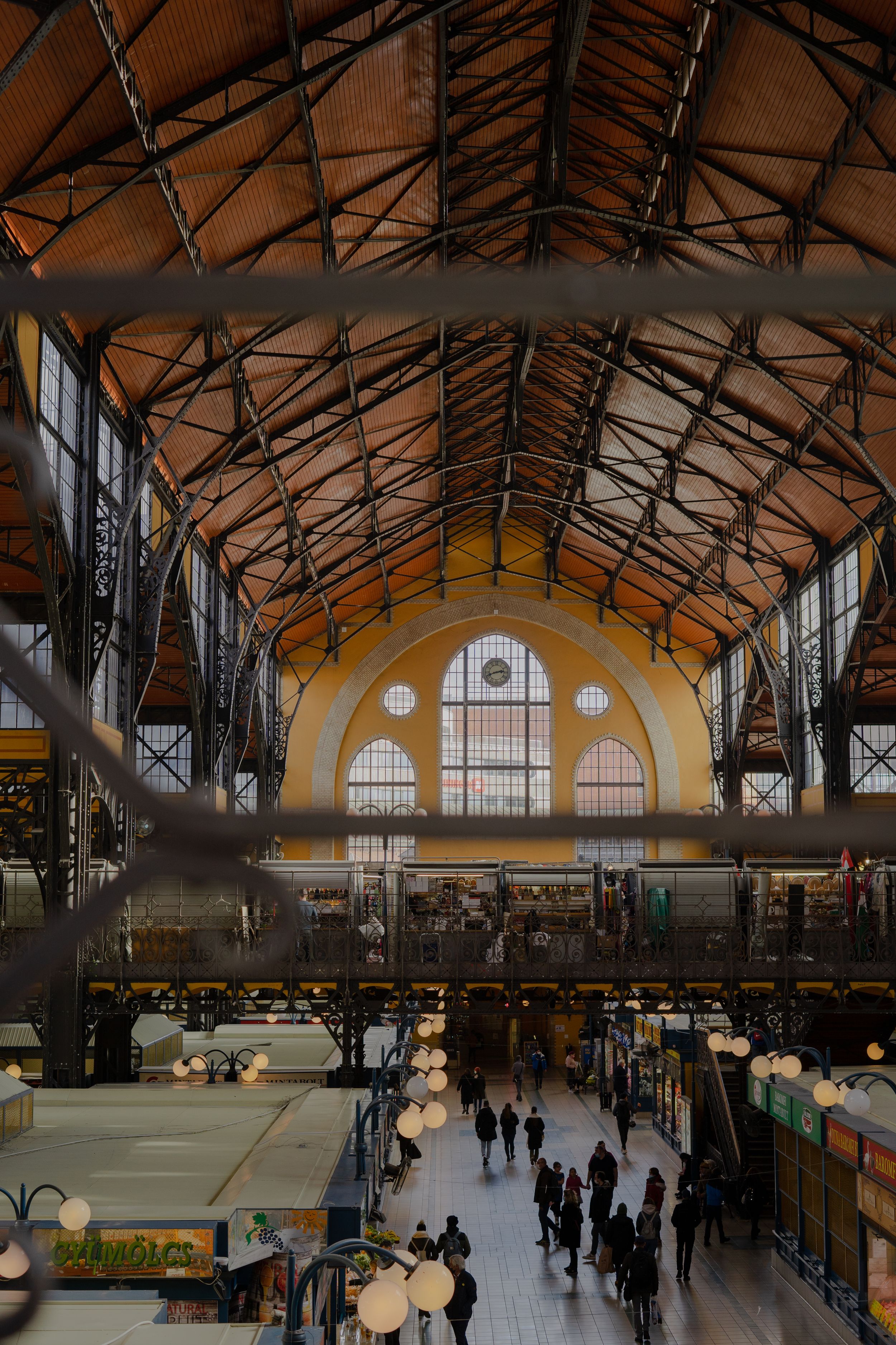 Interior view of a grand market hall with vaulted ceiling, ornate industrial architecture and yellow arched windows.