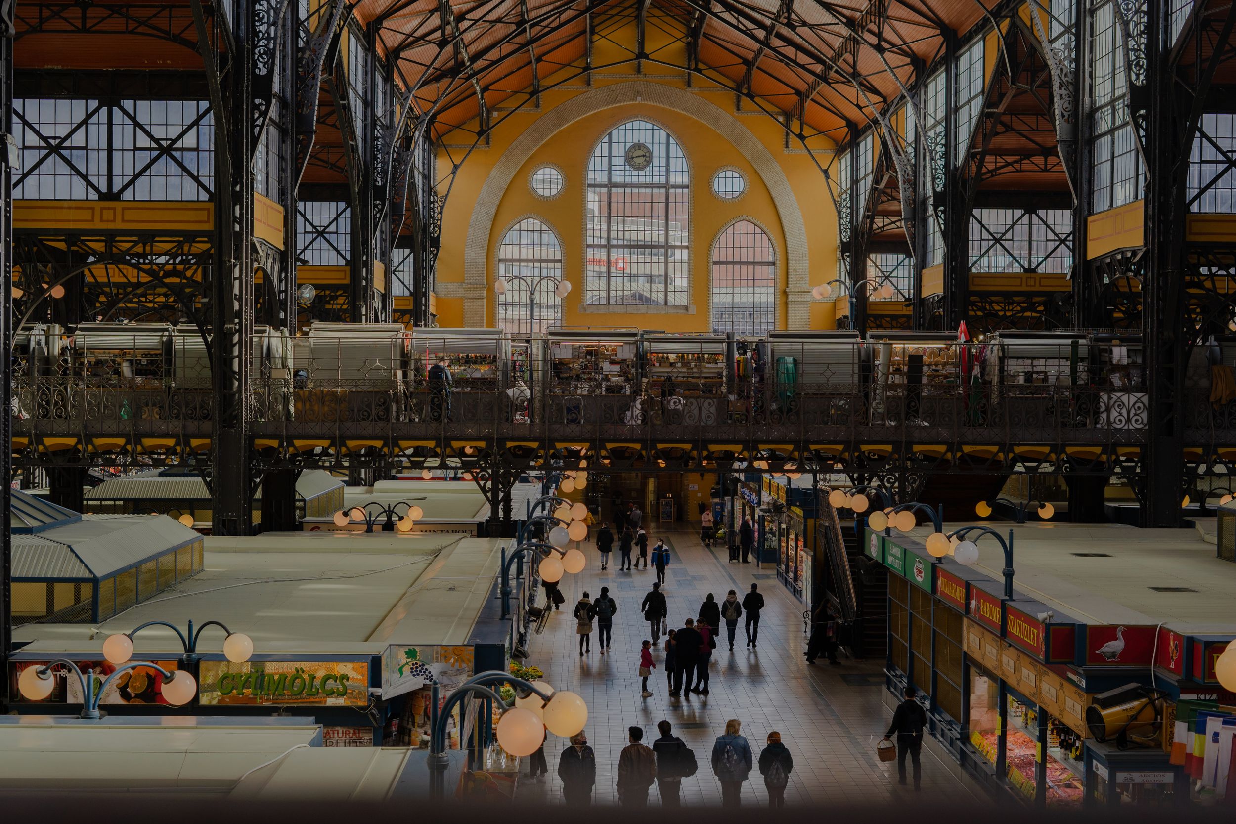 Interior view of the historic Great Market Hall in Budapest with its grand arched windows and visitors browsing vendor stalls.