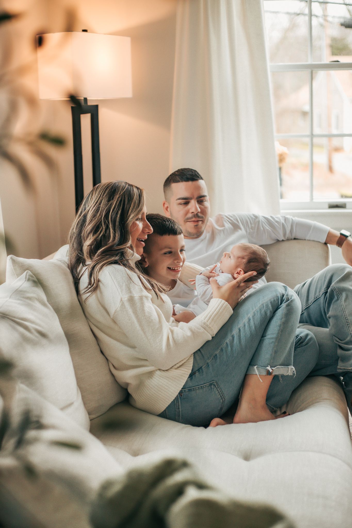 family cuddling on couch holding their newborn baby