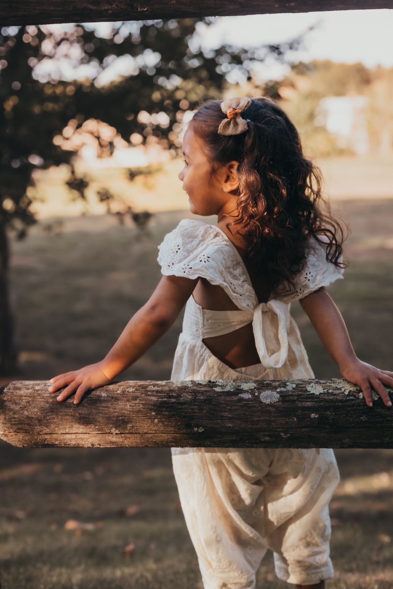 girl leaning on wooden fence staring off into the sunset