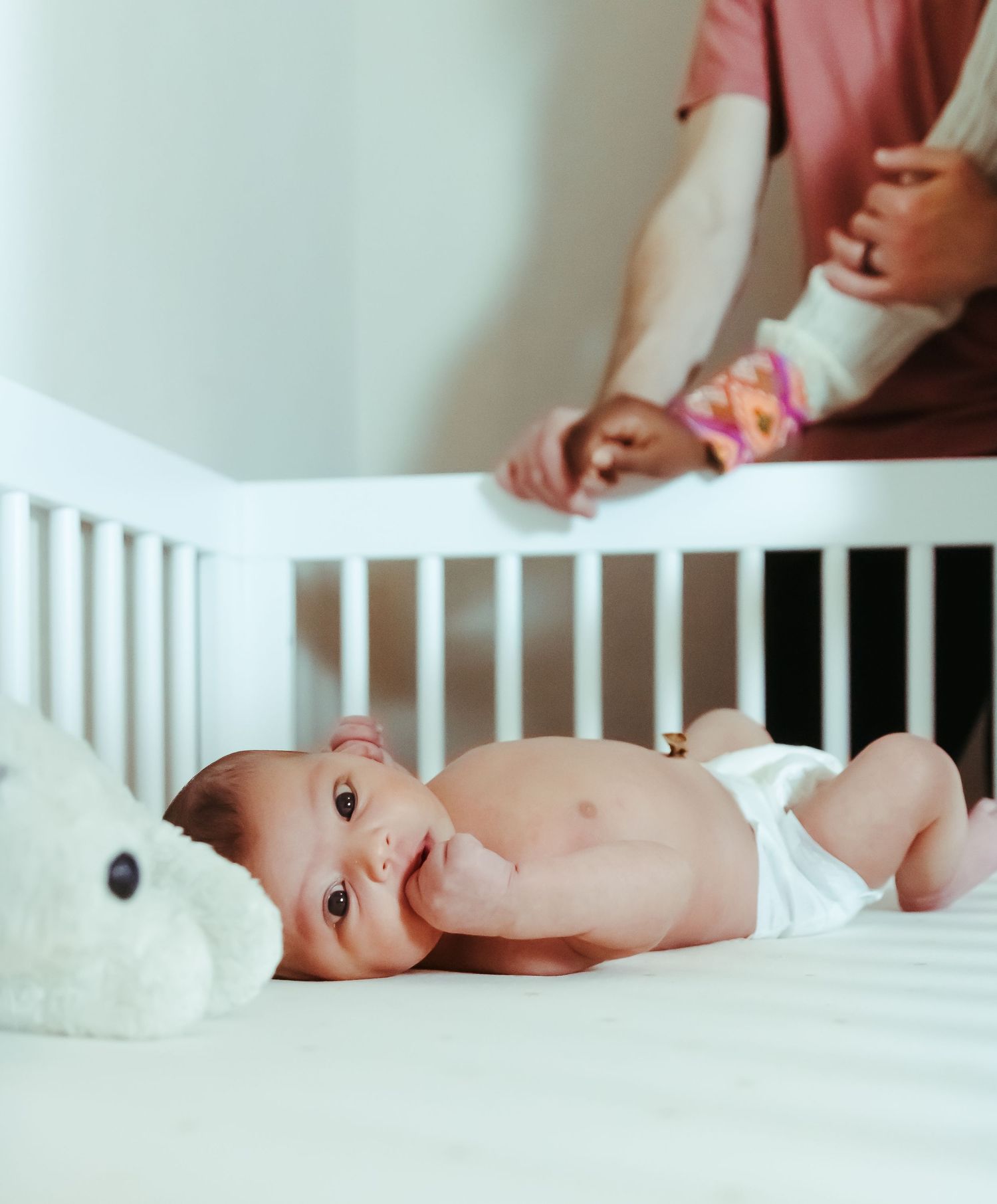 Newborn session with infant in crib while parents look down at her.