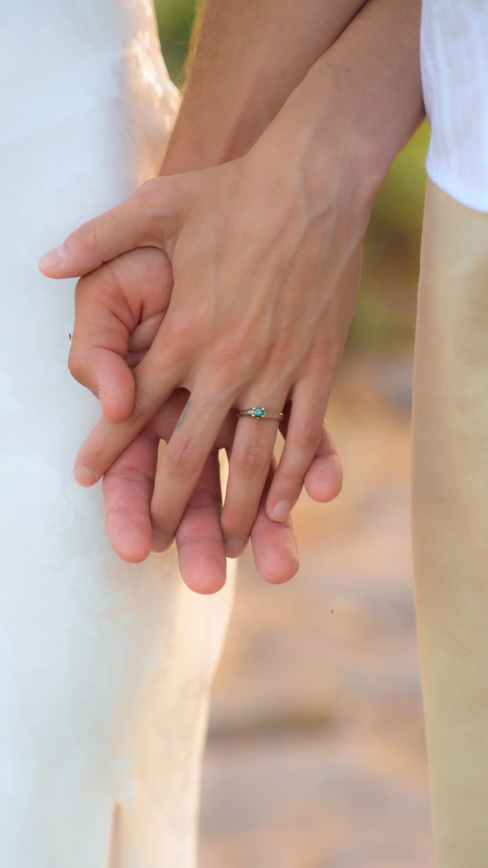 Close-up of couple holding hands showing engagement ring with blue gemstone in outdoor setting.
