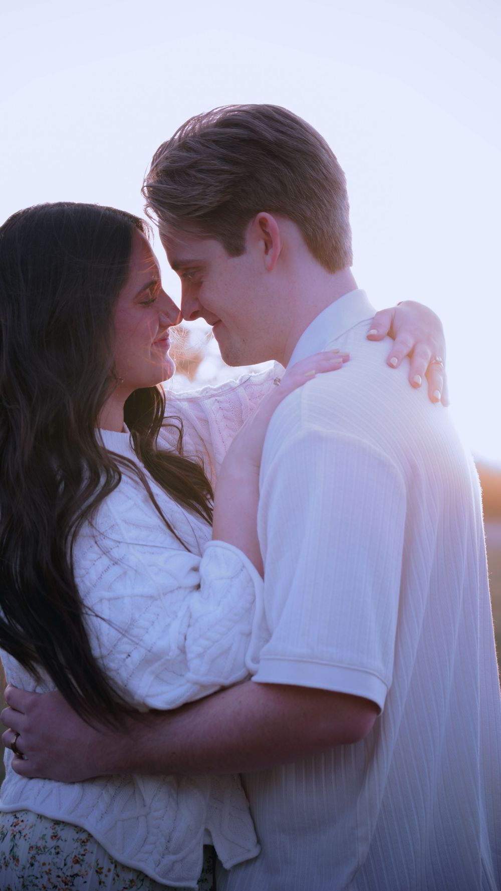 A couple in white clothing embraces intimately against a bright sunlit background creating a romantic silhouette effect.
