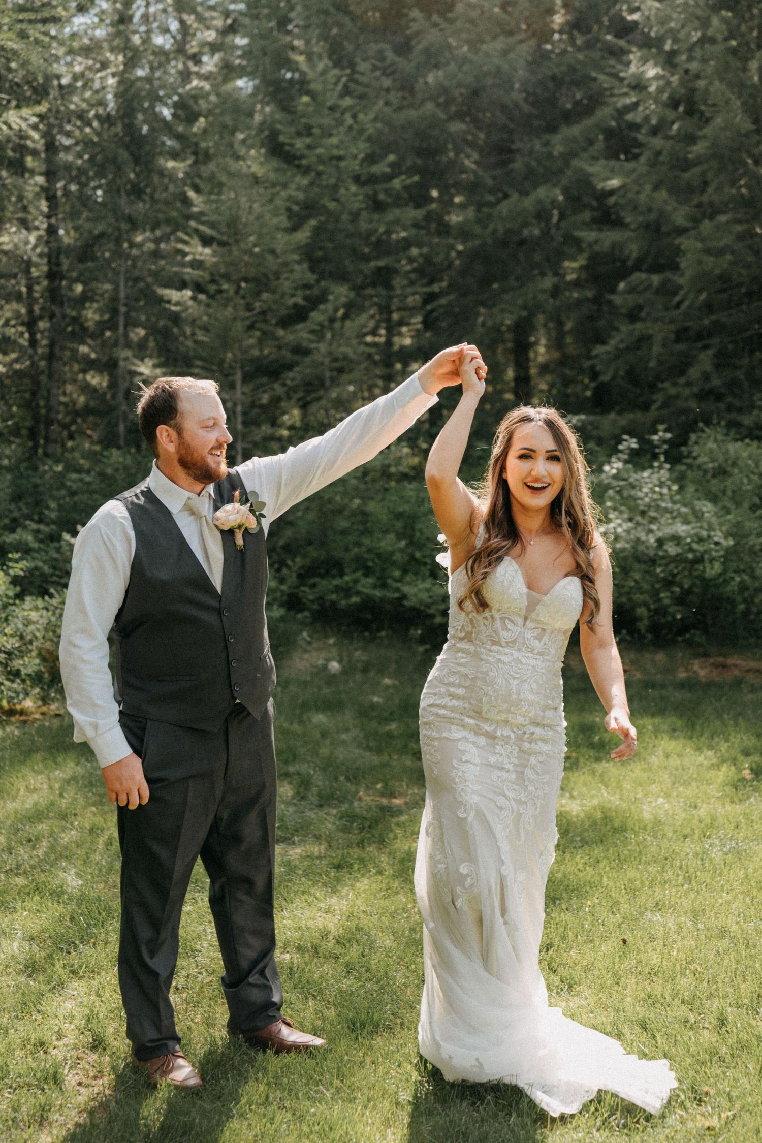 A joyful wedding couple dancing together on grass with evergreen trees captured by wedding videographer Jovan Films.