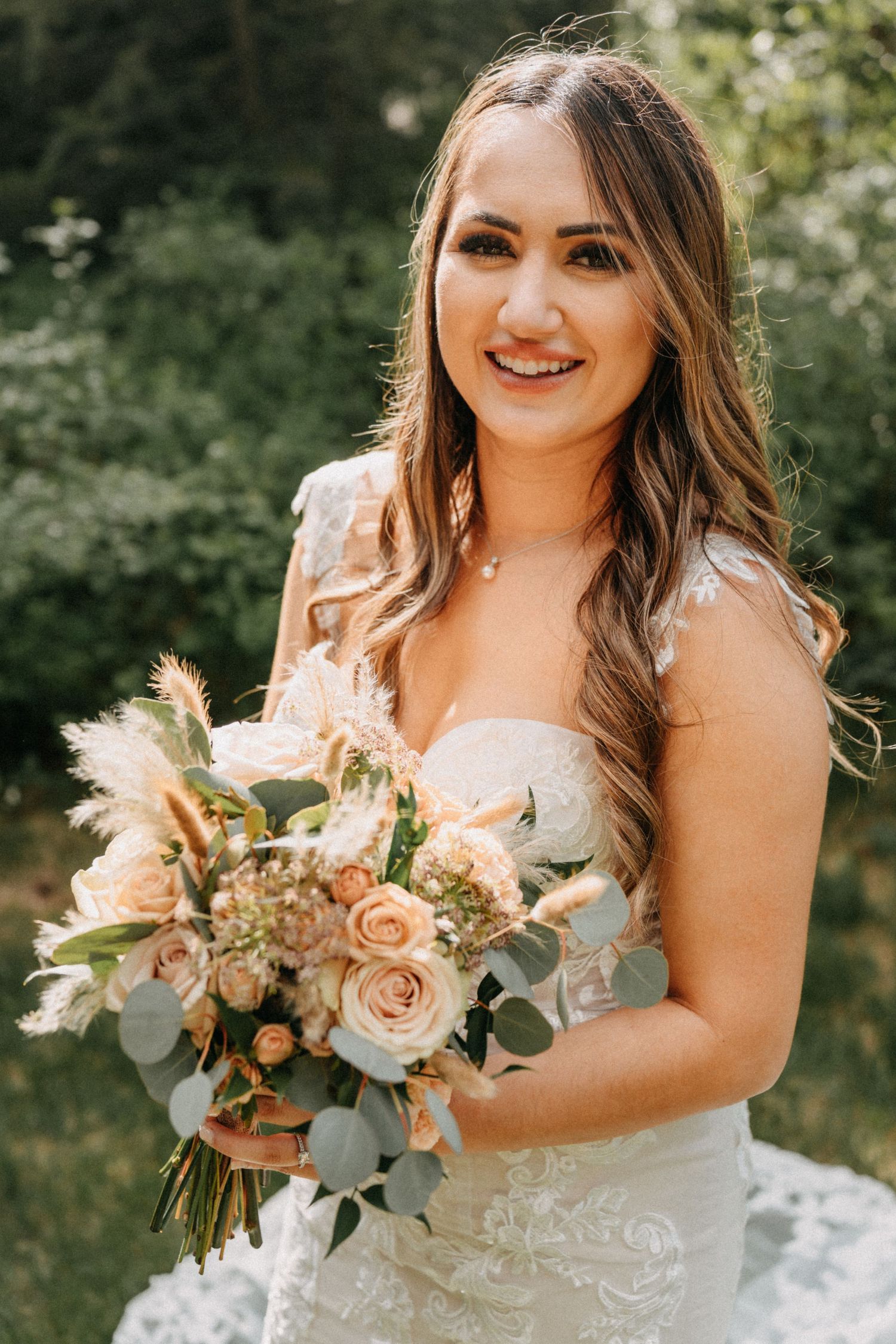 A bride in a white lace wedding dress holds a beautiful bouquet of peach roses and pampas grass captured by wedding videographer Jovan Films
