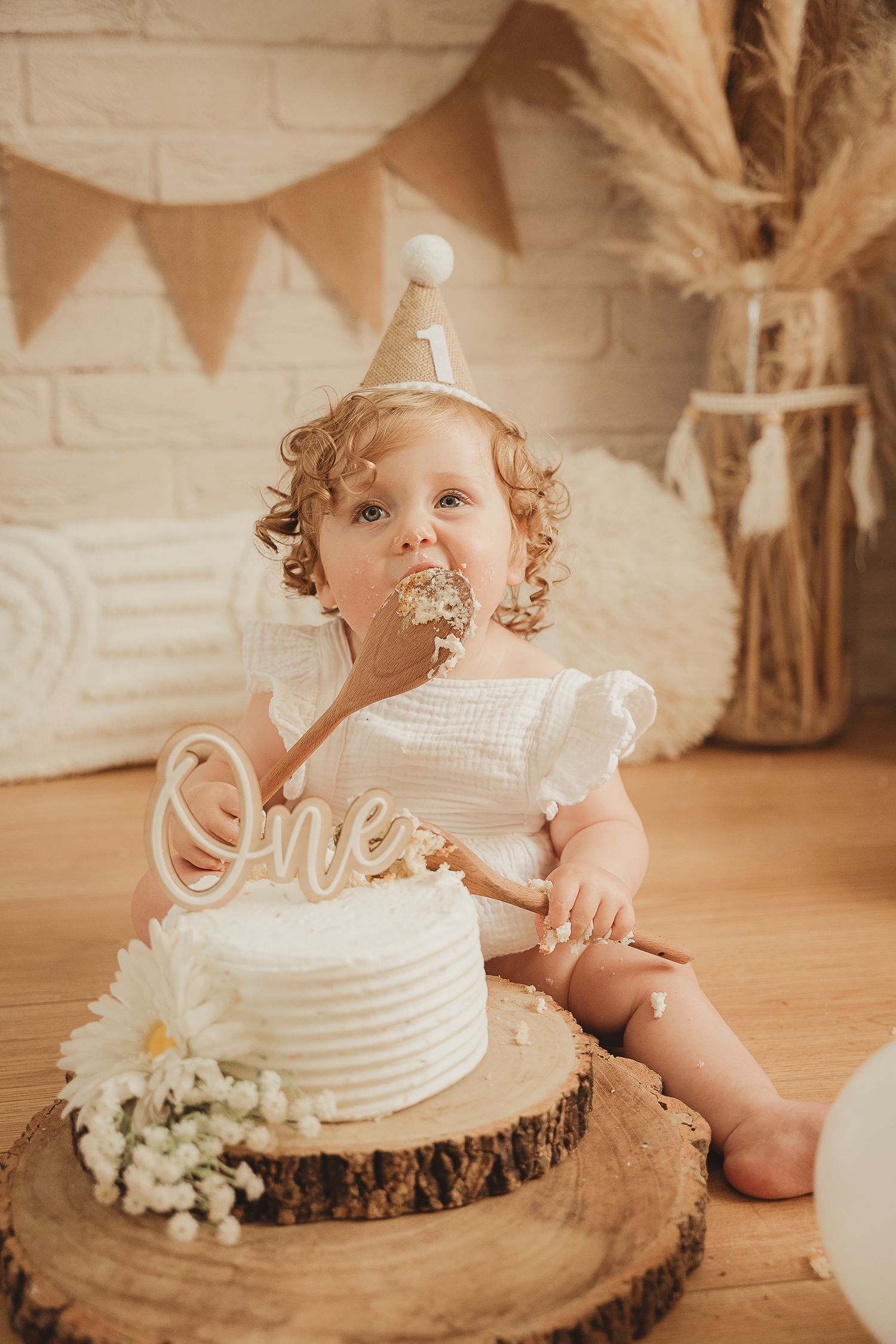 Rustic first birthday celebration with white cake on wood slice, pampas grass decor and neutral bunting backdrop.
