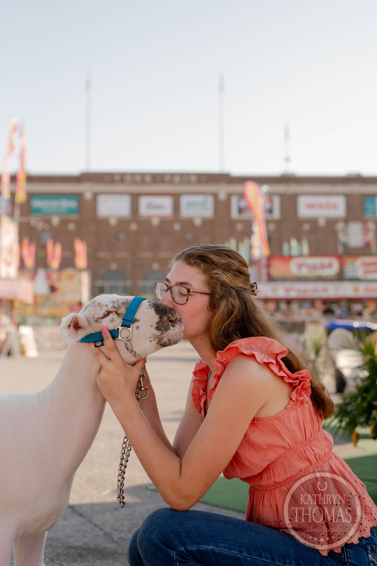 Woman in coral top playing with sheep at carnival fairground.