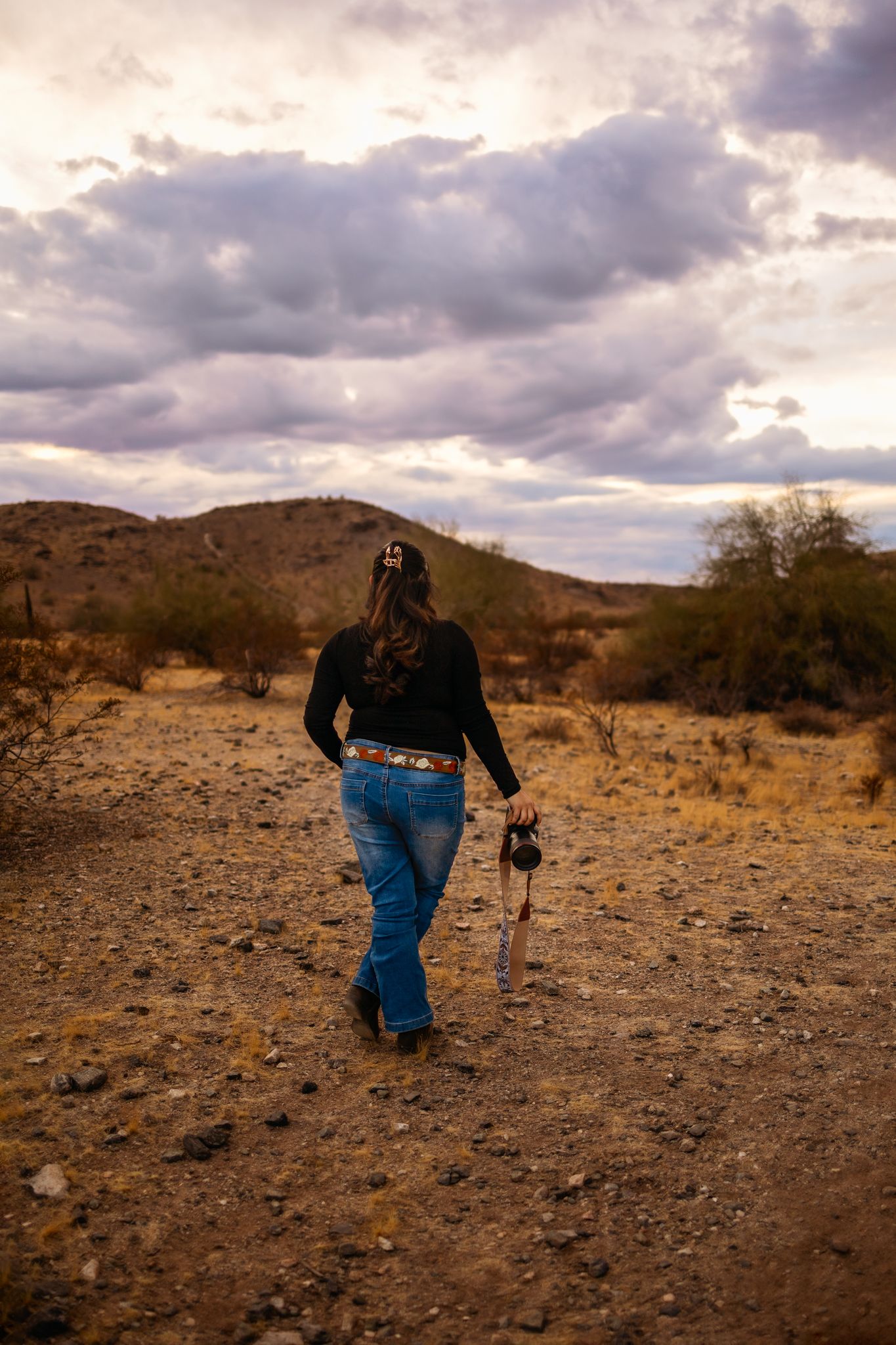 Photographer walking on desert trail with camera during dramatic cloudy sunset in Phoenix Arizona