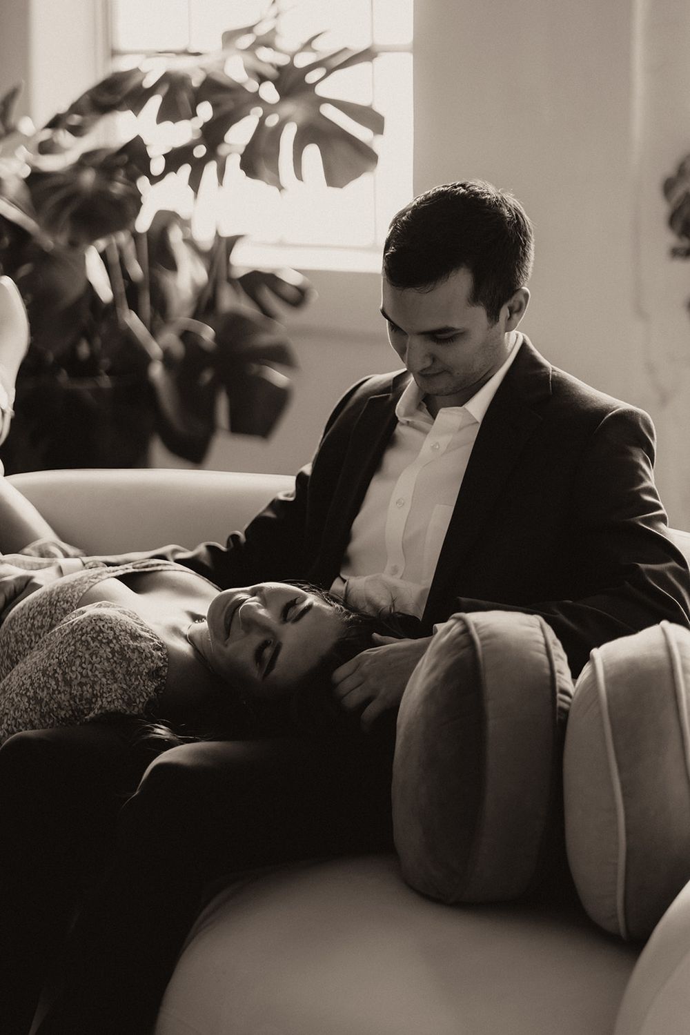 Black and white photo of a couple relaxing on a sofa surrounded by lush indoor plants.