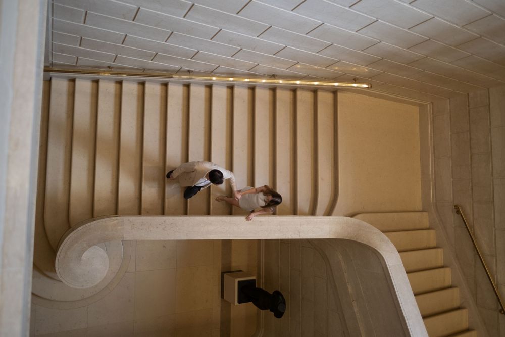 Aerial view of couple walking down elegant curved staircase in modern building.