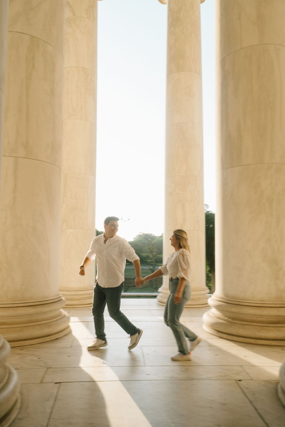 Couple holding hands and walking between grand white marble columns at the Jefferson Memorial.