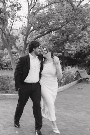 Couple in black and white photo smiling and walking together in a tree-lined park setting.