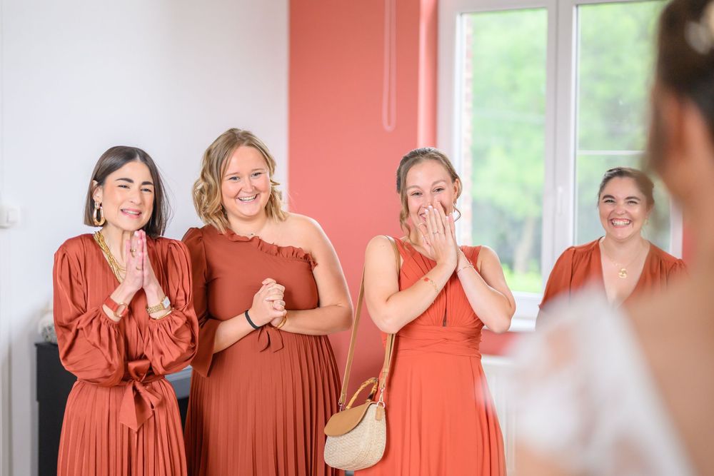 Bridesmaids in coral-colored dresses react emotionally during a wedding moment.