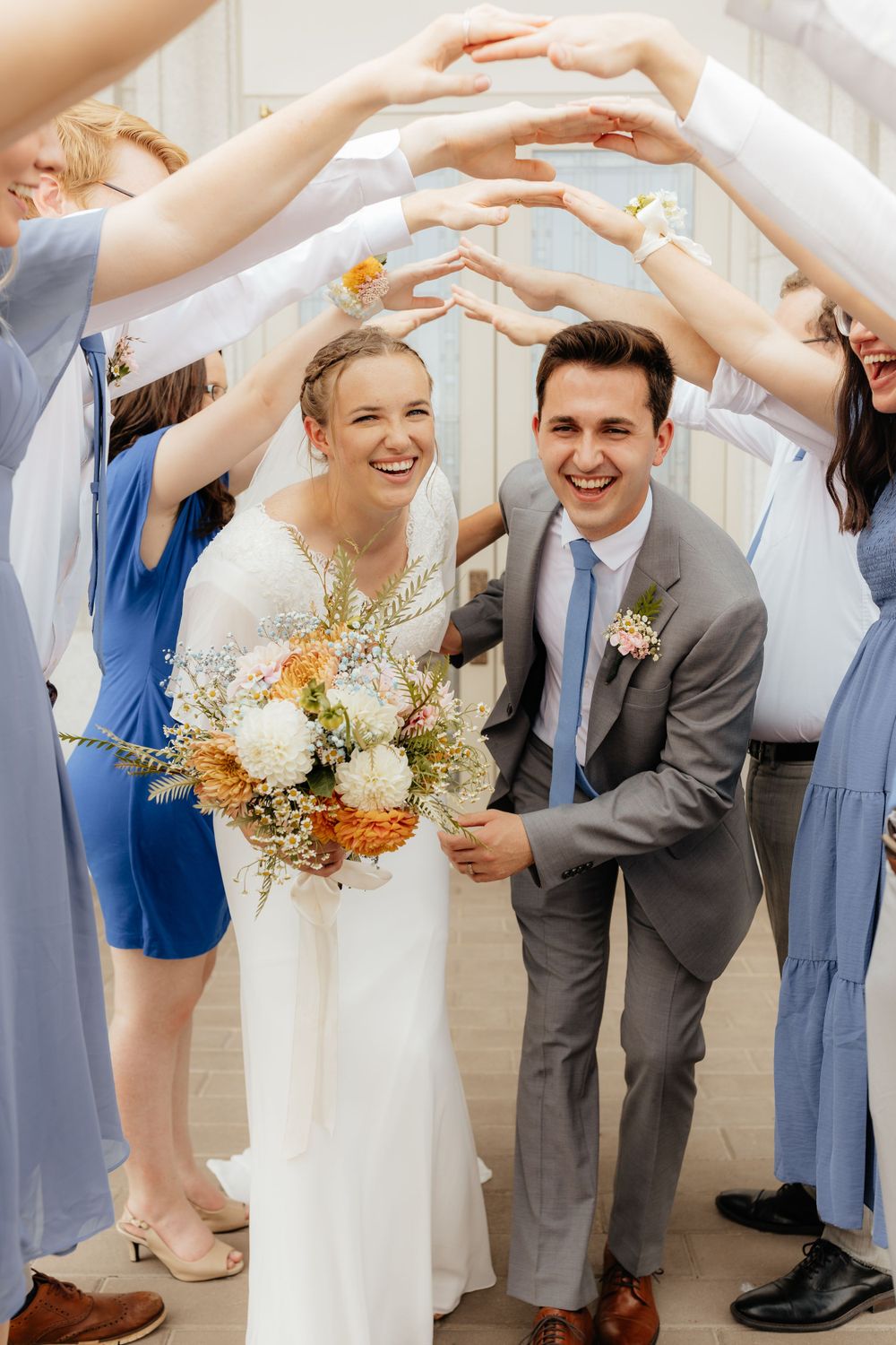 Smiling bride and groom walk under an arch of raised hands formed by wedding guests indoors.