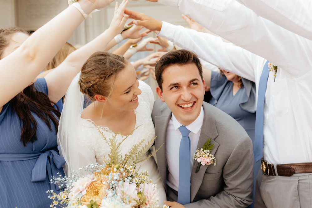 Smiling bride and groom walk under arch of raised hands formed by wedding party.