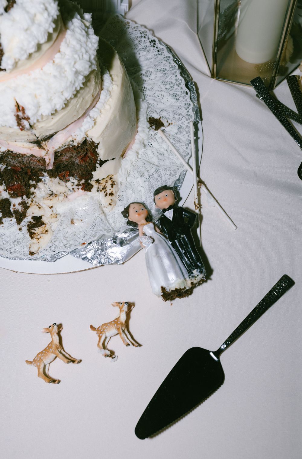 Wedding cake topper figurines with deer decorations beside a cake server on a white tablecloth.