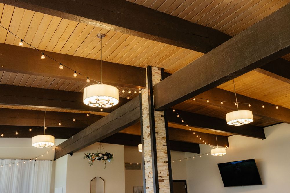 Rustic wedding venue interior with wooden beam ceiling and warm pendant lighting.