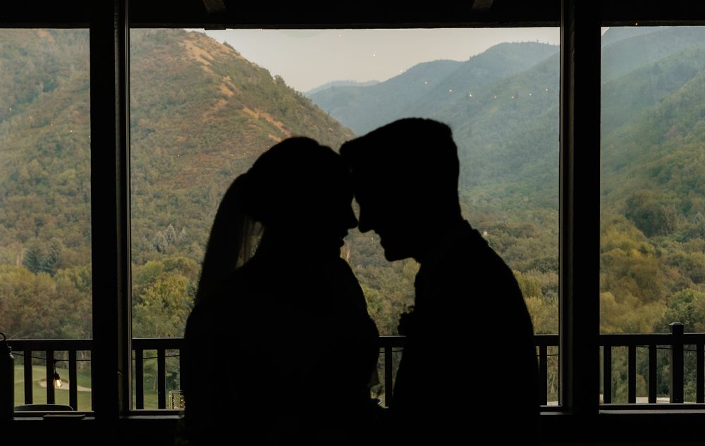 Silhouette of bride and groom facing each other with a scenic mountain forest view behind them.