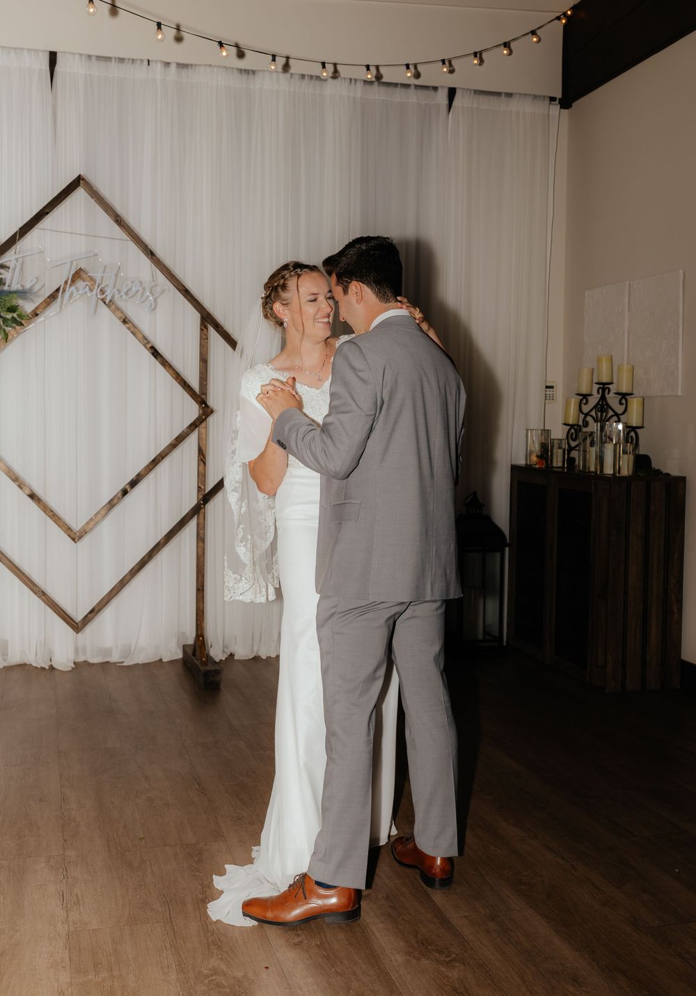 Newlyweds sharing intimate first dance in front of geometric wooden backdrop decor.