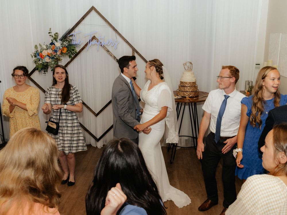 Bride and groom share first dance surrounded by guests at elegant indoor wedding reception with floral backdrop.