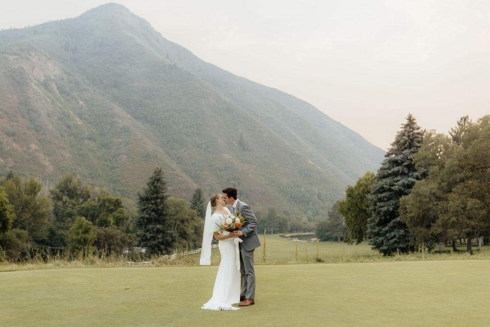 Bride and groom sharing a romantic moment on a golf course with a stunning mountain landscape.