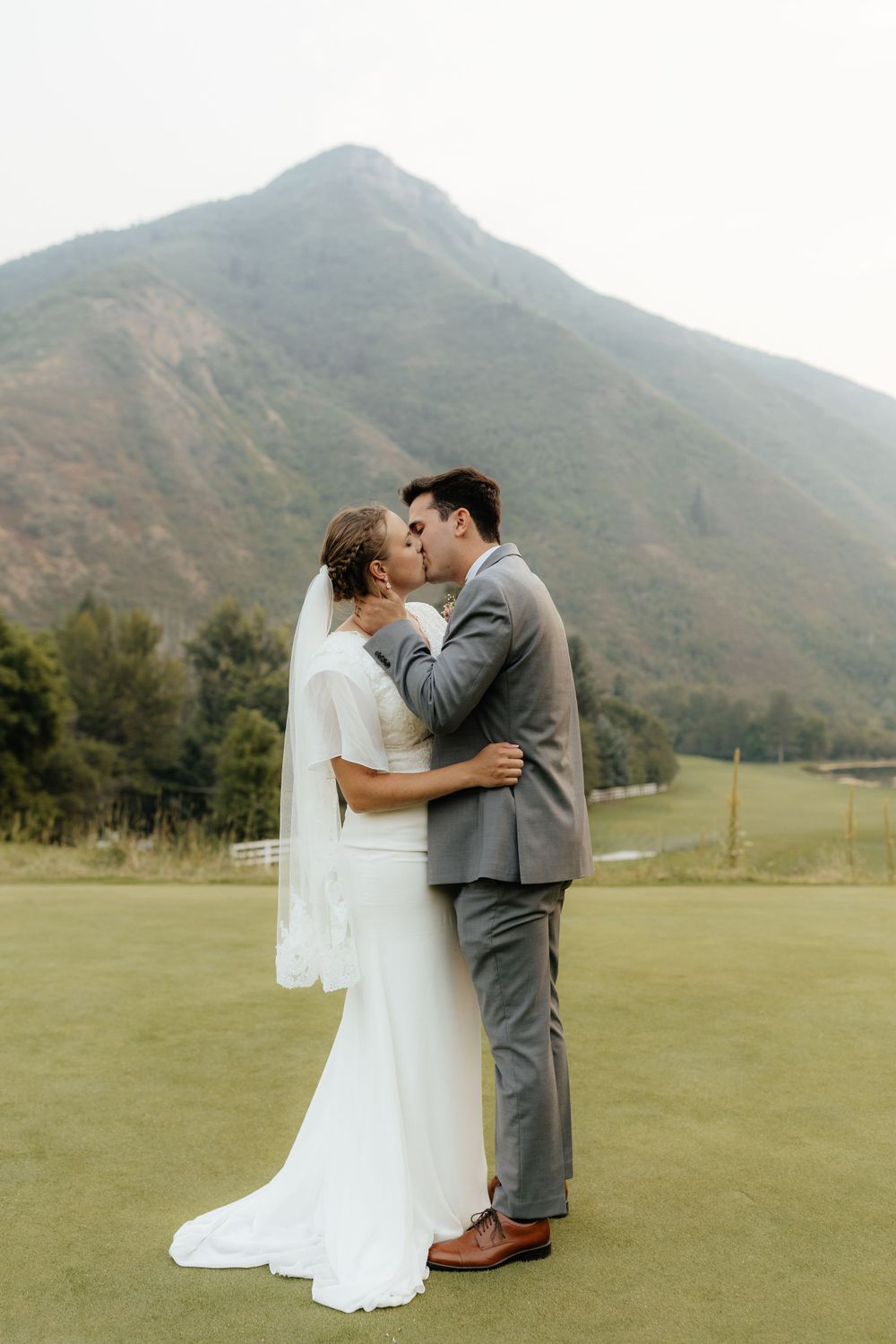 Bride and groom kissing on a lush green golf course with a dramatic mountain in the background.