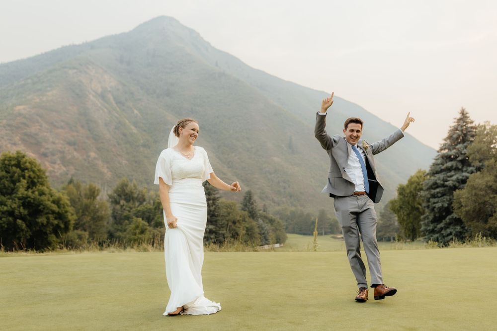 Joyful bride and groom celebrating on a golf course with arms raised against a mountain backdrop.