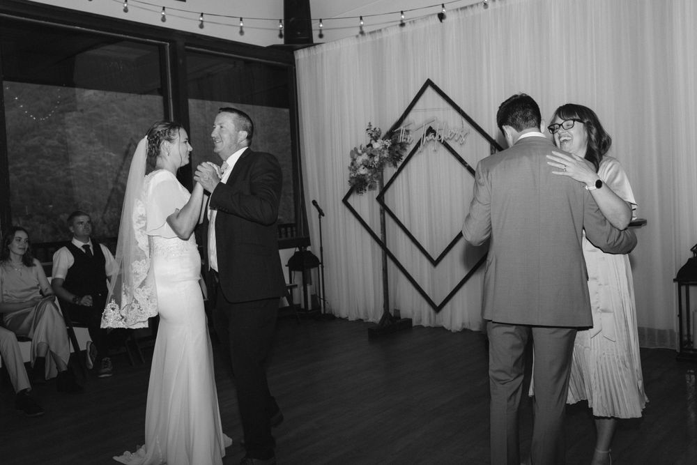 Black and white photo of bride and groom sharing parent dances at wedding reception.