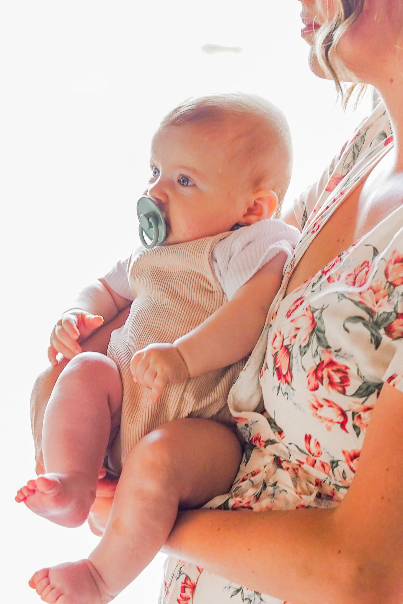 Baby with pacifier wearing ribbed onesie being held against floral print.
