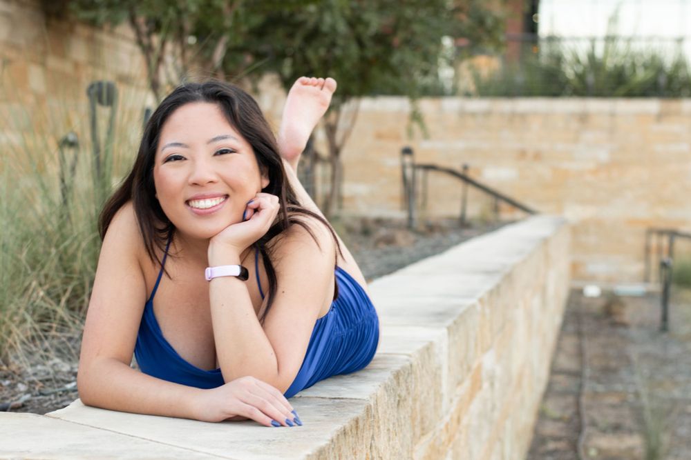 Casual portrait on stone wall with natural landscaping in background.