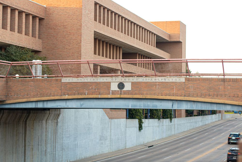 Modern architectural detail of curved concrete bridge structure with brick building in background.