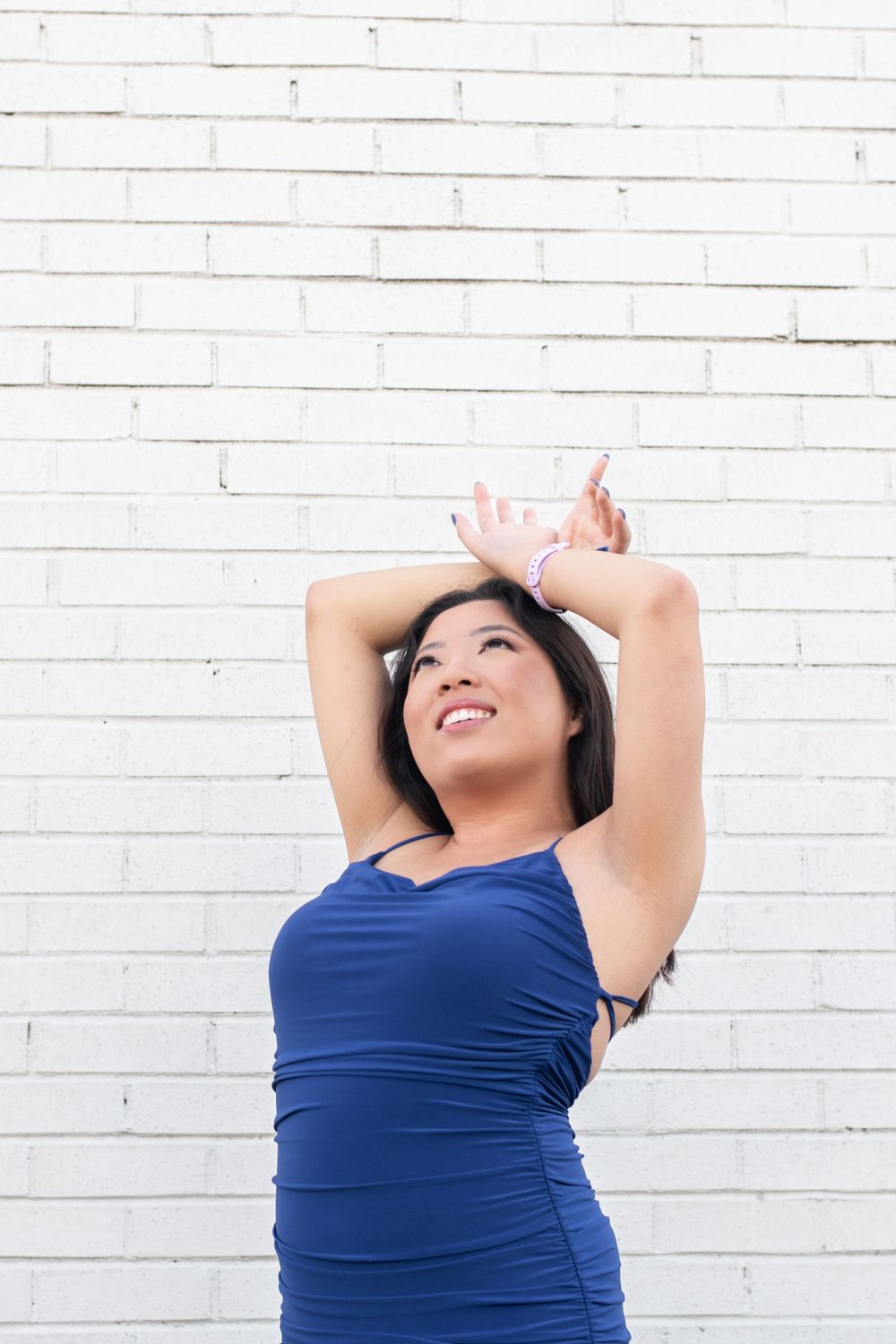 Woman in blue top poses expressively against white brick wall background.