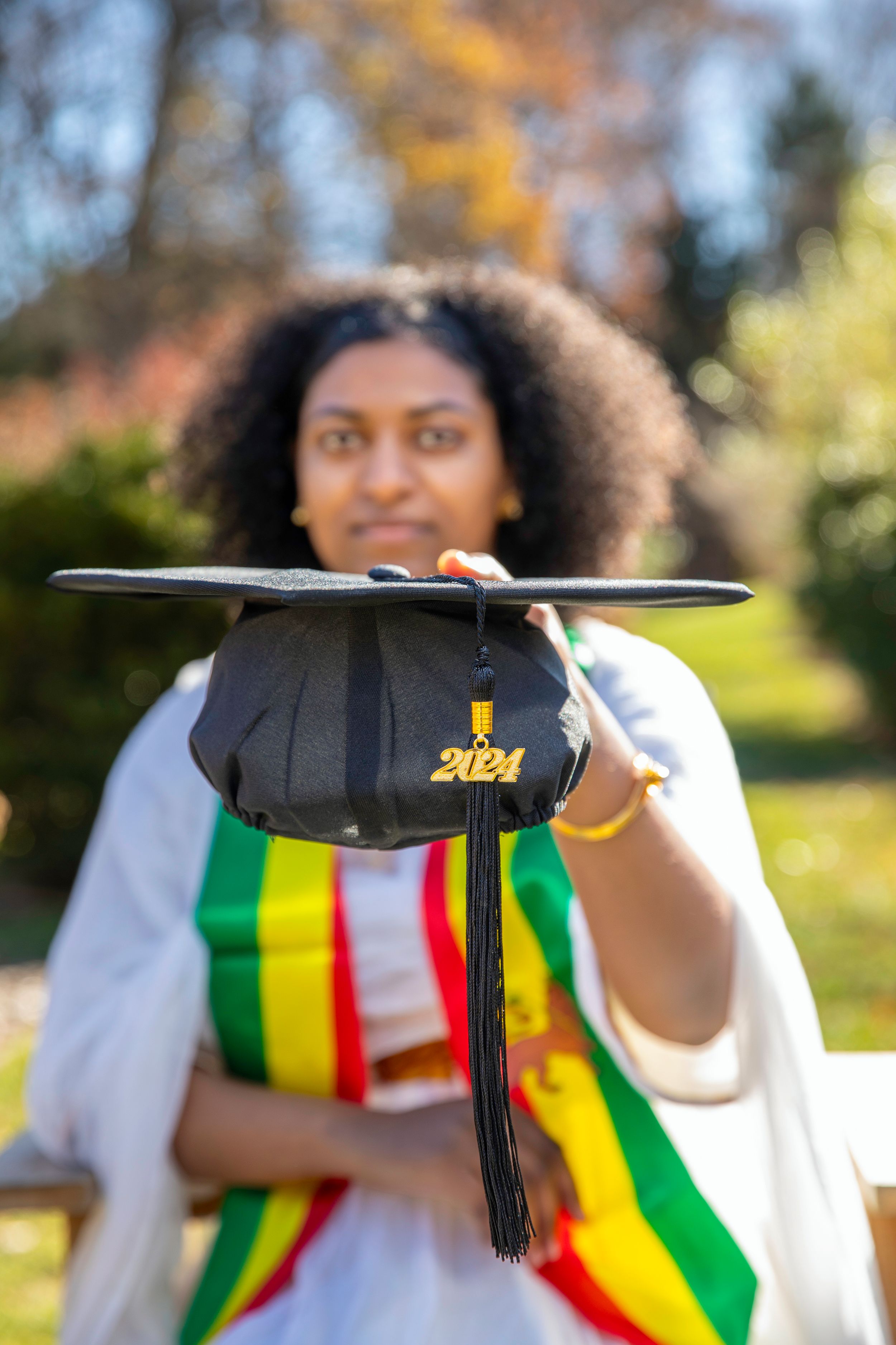 Close-up of 2024 graduation cap with colorful stole in outdoor setting.