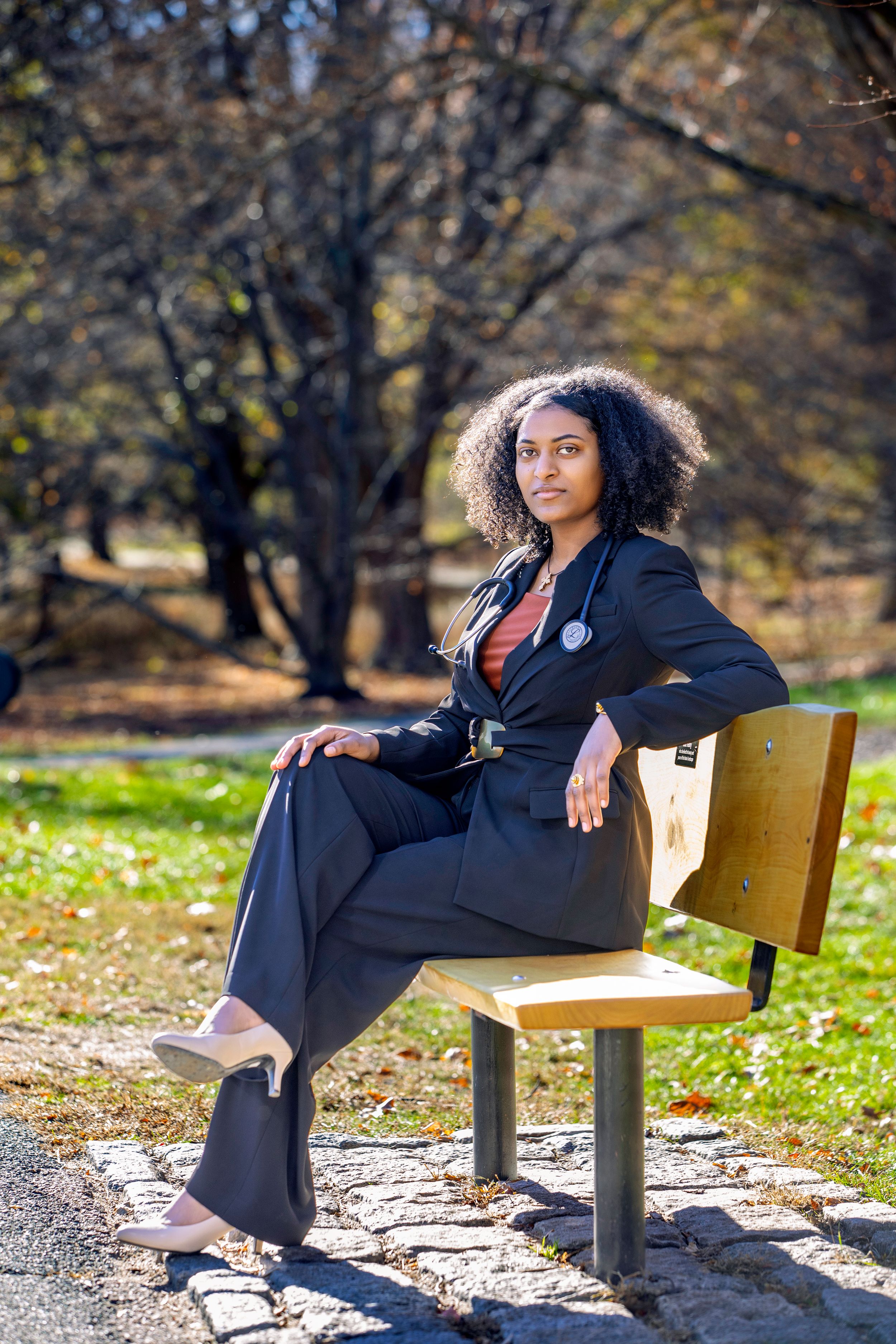 Professional in black suit sitting on park bench in autumn setting.