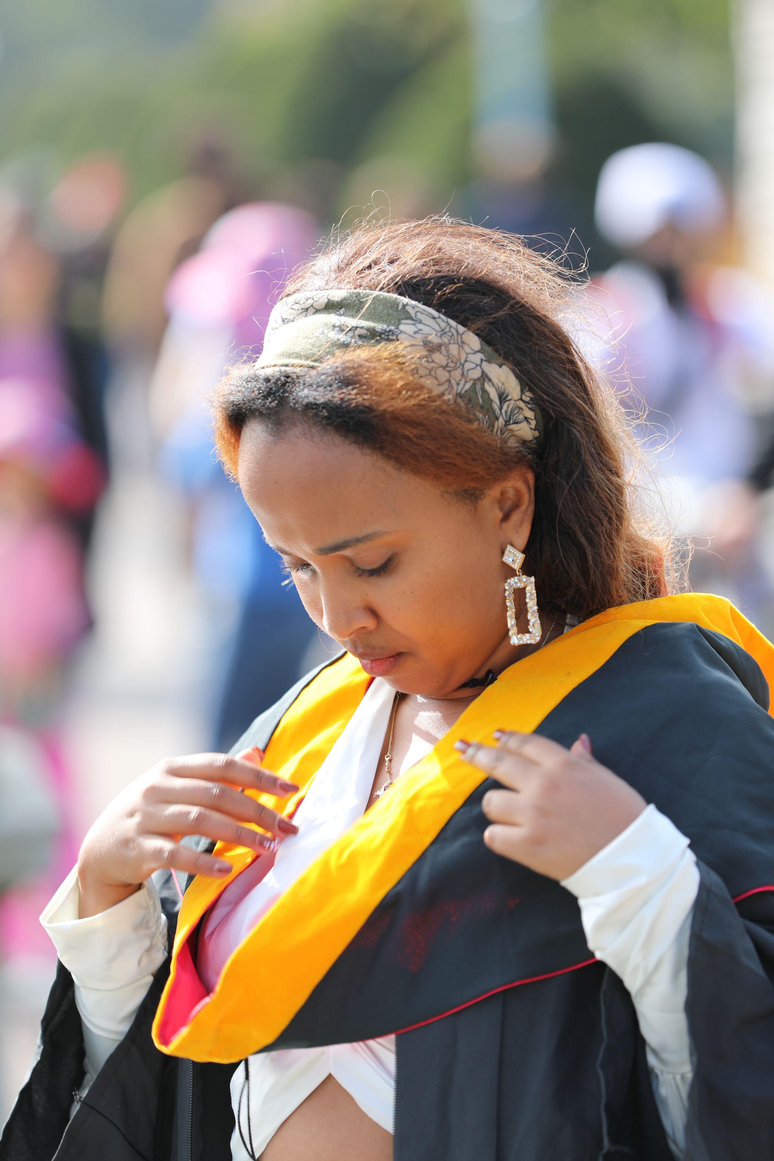 Graduate adjusting academic stole during outdoor graduation ceremony.
