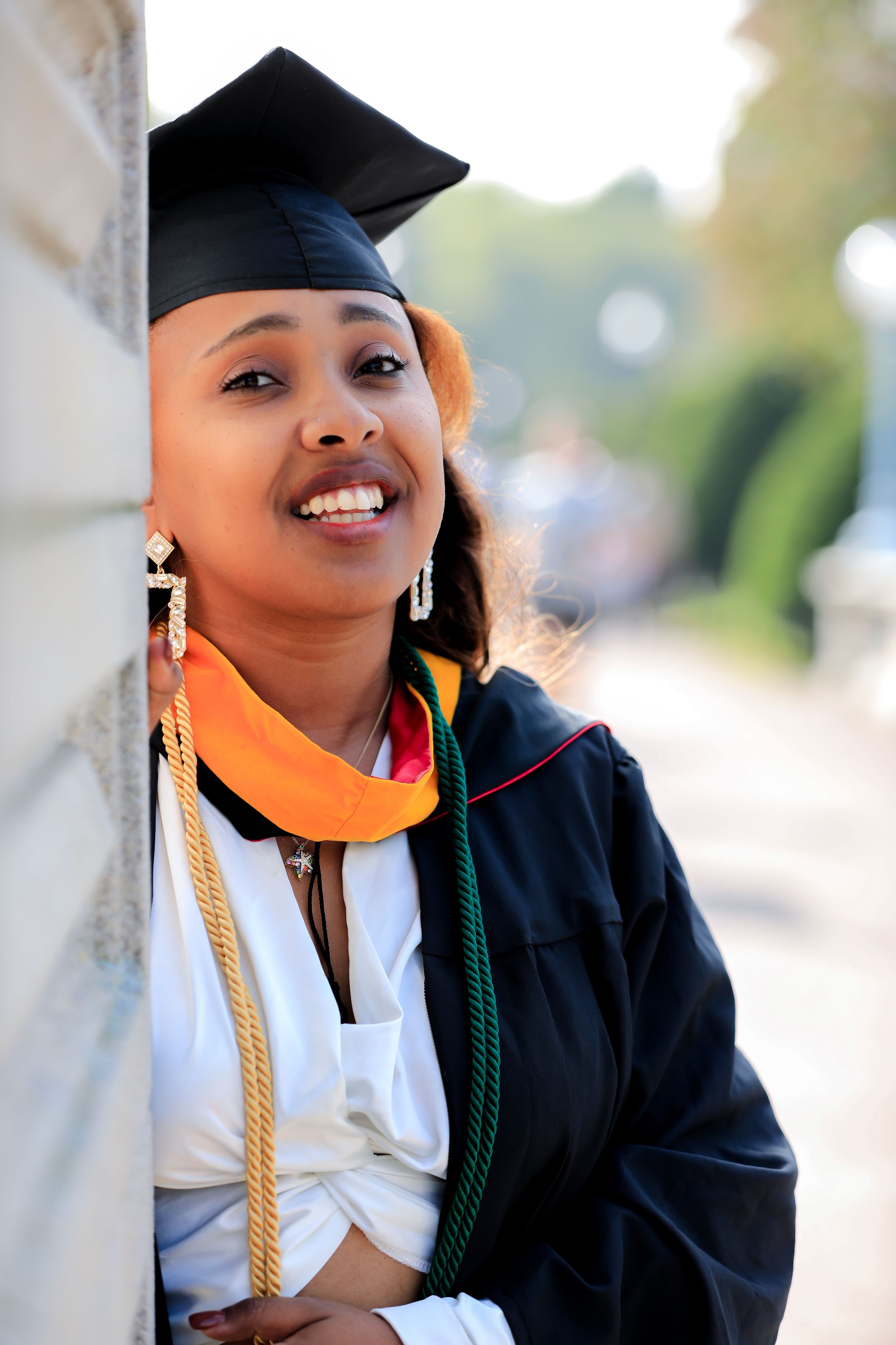 Graduate in cap and gown smiling against wall during graduation ceremony.