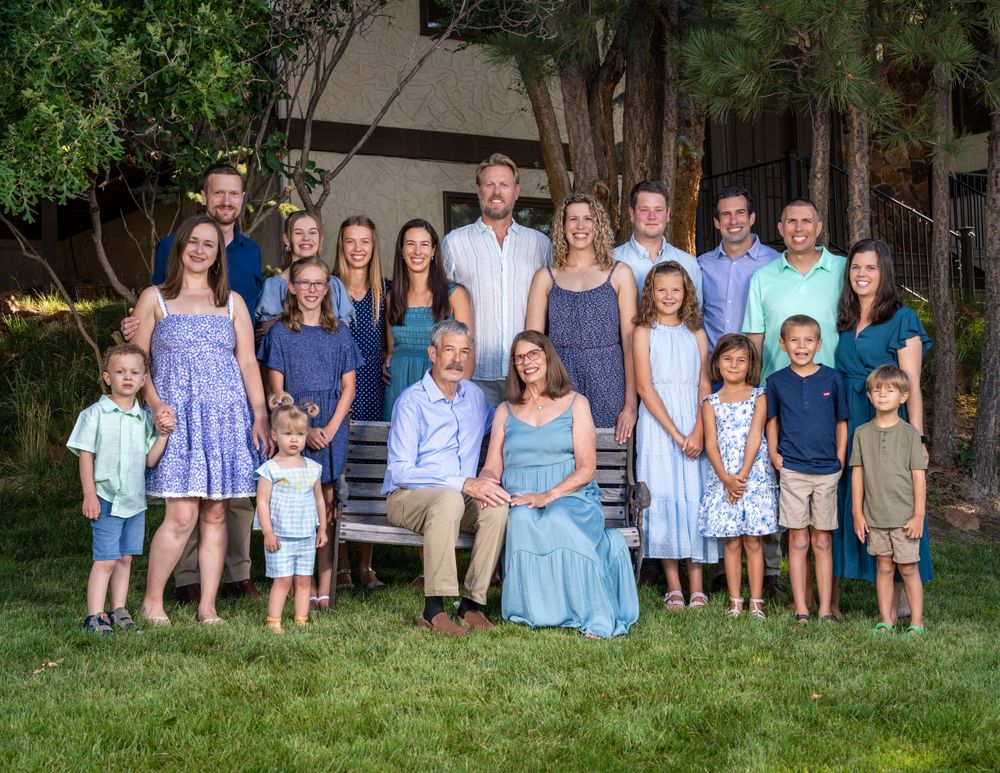 Large family group posed together outdoors on wooden bench wearing coordinated blue and white outfits.