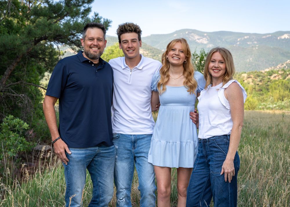 Family portrait of four people standing together outdoors with mountain landscape in background.