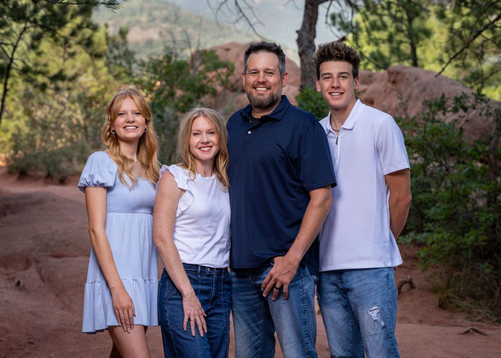 Family of four posing together on hiking trail with mountain scenery behind them.