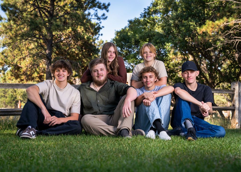 Group of young friends sitting casually together on grass in outdoor setting.