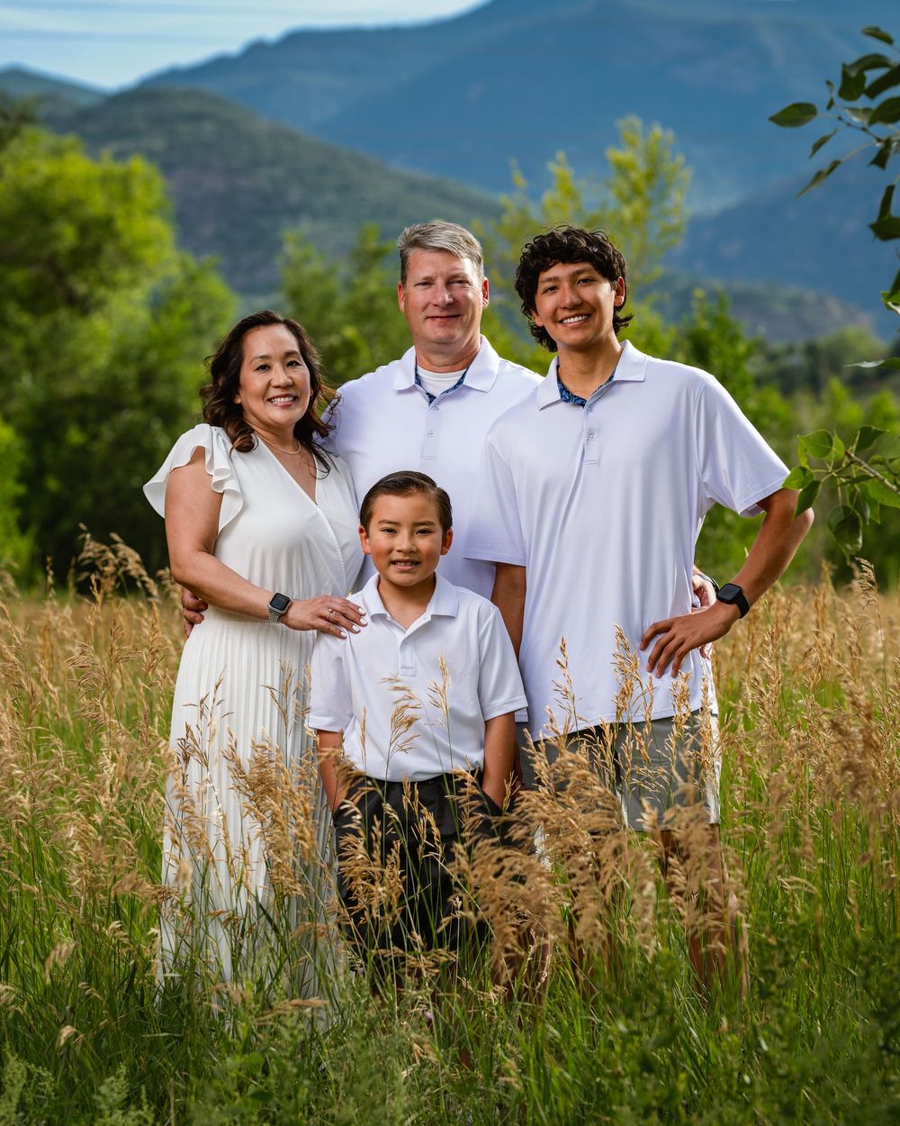 A group stands together in a sunny meadow field with mountain ranges visible in the background.