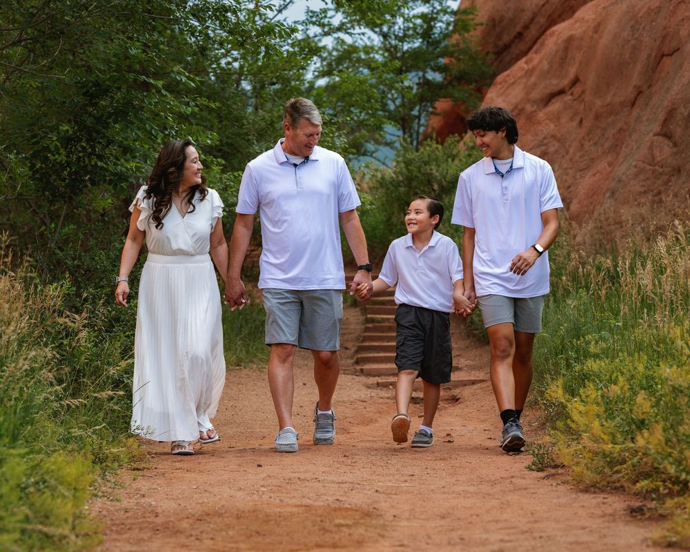 A group dressed in white and blue walks together on a red dirt trail surrounded by green foliage.