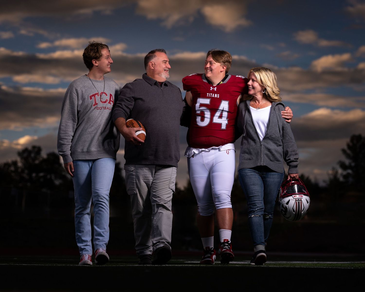 A family group poses together at sunset on a football field with dramatic cloudy sky in the background.