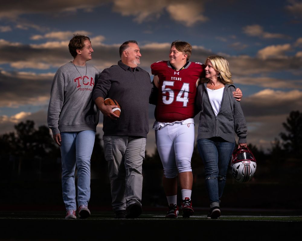 A family group poses together at sunset on a football field with dramatic cloudy sky in the background.