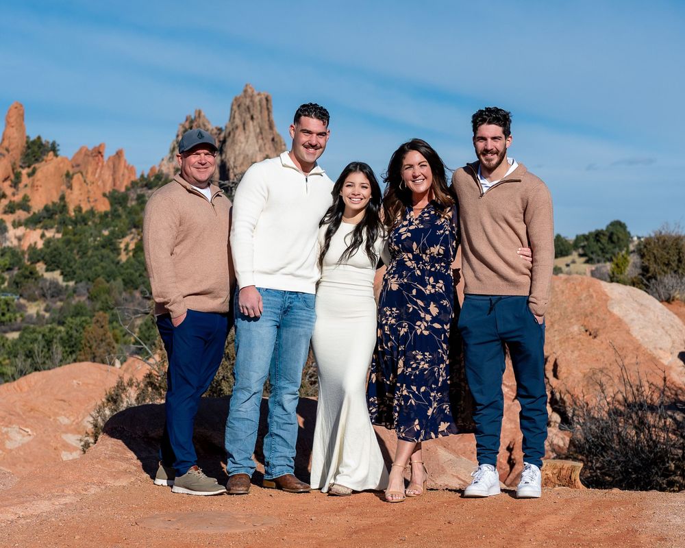 A group of people sitting together on red rocks at Garden of the Gods park in Colorado on a sunny day.