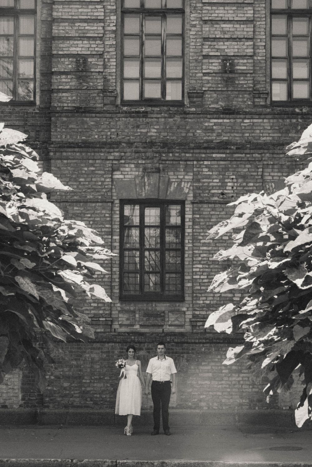 Vintage black and white photograph of a brick building with snow-covered plants.
