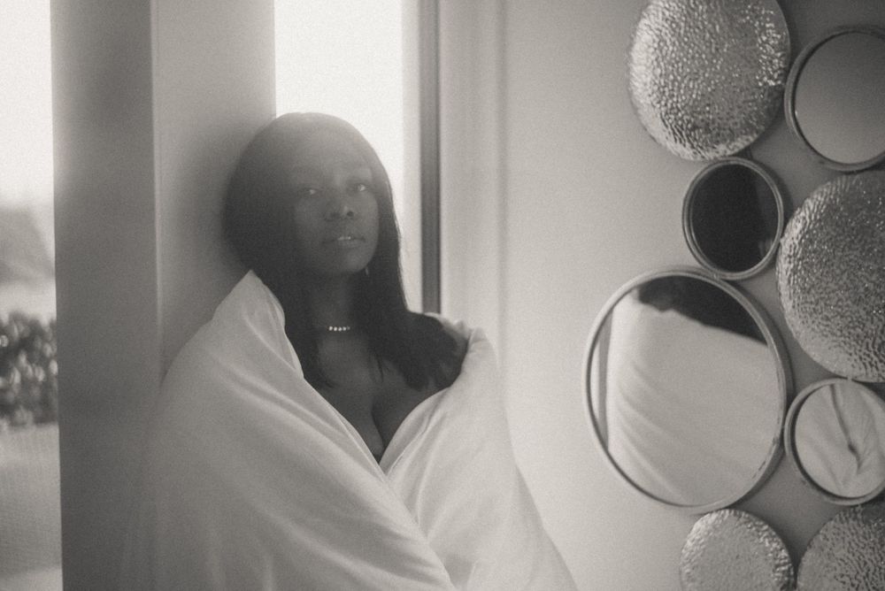 Moody black and white portrait showing figure wrapped in white fabric near circular wall decorations.